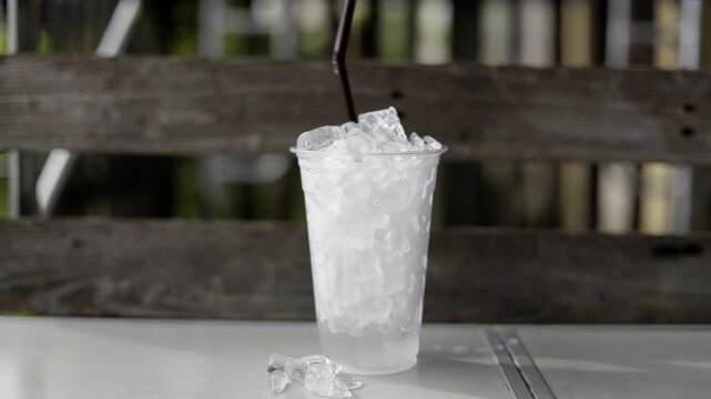 Ice Melt In Plastic Glass, A cinematic film clip of ice melting in plastic glass, cubes shrinking in clear droplets under soft light, perfect for climate awareness film or beauty documentary.