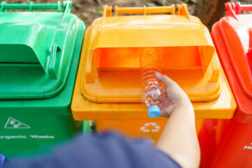 Woman recycling a plastic bottle at public waste separation bins.