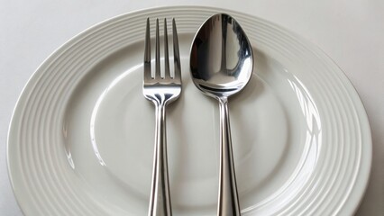 A polished fork and spoon are elegantly placed on a pristine white plate, ready for a refined dining experience.