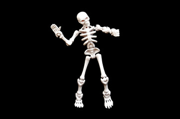 A small, articulated human skeleton model with red eyes, standing upright on a stark black background. Concepts of anatomy, biology, Halloween, fear, science, education, medical, spooky, and death.