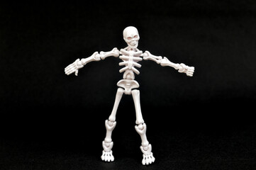 A small, articulated human skeleton model with red eyes, standing upright on a stark black background. Concepts of anatomy, biology, Halloween, fear, science, education, medical, spooky, and death.