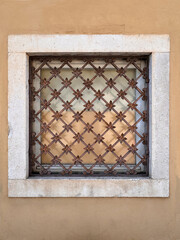 old ornate rusty criss cross grill on window with stone frame against rendered wall on building exterior in Croatia