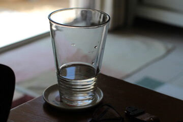 Empty glass on a table with a saucer, natural light and reflections