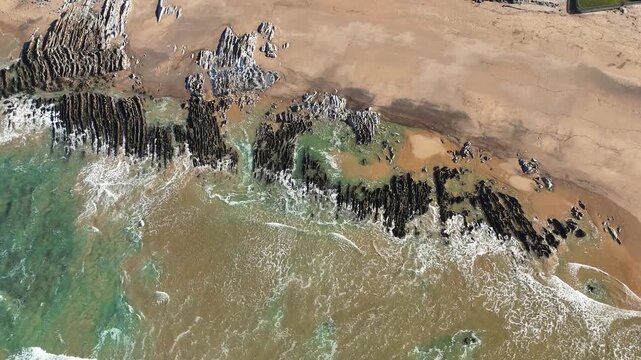 Vagues batantes au bord de l'eau sur des roches stri&eacute;es formant des lettres abstraites. contraste sable, roche, paisible, nature, peinture