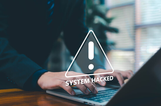 A warning sign showing “System Hacked” over a person typing on a laptop, symbolizing cybersecurity breaches, data threats, hacking incidents, digital risk awareness, and system vulnerability in modern