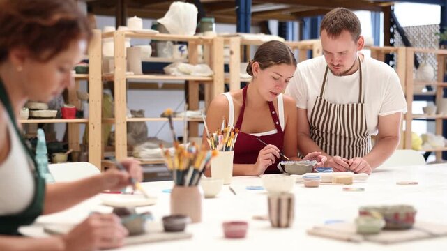 During master class, student paints clay vessel under guidance of male teacher. Mentor is next to student, makes comments and corrects inaccuracies - Powered by Adobe