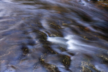 Close view of moving water forming smooth streaks and gentle motion over submerged stone