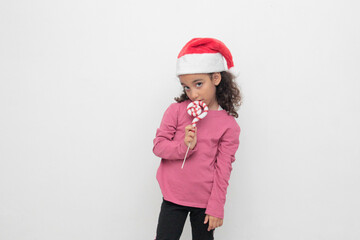 4-year-old Latina girl with curly brown hair wearing a santa hat sings with a candy cane to celebrate Christmas and New Year