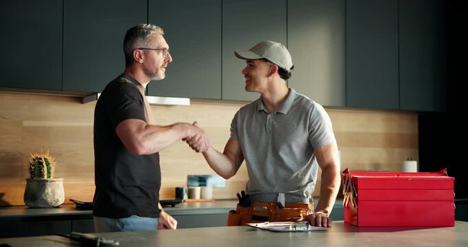 Mature man, plumber and handshake in kitchen with smile, invoice or price for repair service in home. People, maintenance checklist and shaking hands with thanks, happy and solution for leak at house