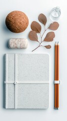 A minimalist flat lay composition featuring stationery and natural elements arranged on a white surface.