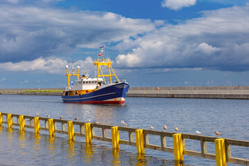 Colorful fishing vessel entering the harbor in Gdynia, Poland with seagulls on a wooden barrier