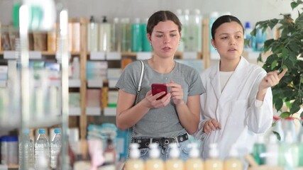 Focused young woman with smartphone in hand looking for something in pharmacy store, asian woman pharmacist helping choosing and making decisions 