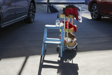 Blue stool with bottle of hand sanitizer next to rolling cart full of clothes and personal items....