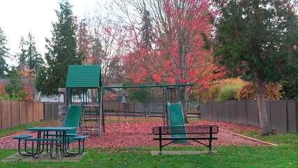 A playground in the area between the houses. Red tree leaves move in the wind in autumn.