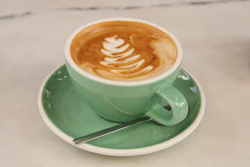 Warm coffee cup with latte art on a green saucer