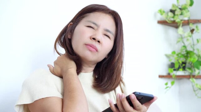 Asian woman suffering from neck and shoulder pain due to prolonged mobile phone use and poor posture. Concept of tech neck, smartphone overuse, internet addiction, and modern lifestyle health issues