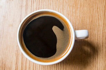 Cup of coffee americano on wooden background, top view. Espresso in white ceramic cup. Black coffee...