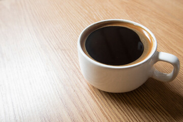 Black Coffee in a white cup on a wooden table. Light brown background.