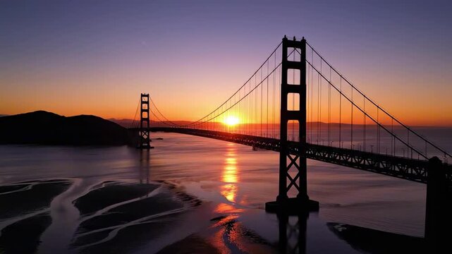 aerial bridge - A stunning aerial view of a suspension bridge at sunset, with vibrant hues of orange and purple illuminating the sky, reflecting off the water and highlighting the landscape
