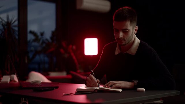 A young man writing in a notebook at a cozy home desk, journaling in warm evening light. Calm atmosphere, self-reflection, focus, and quiet lifestyle moments in a comfortable living room.
