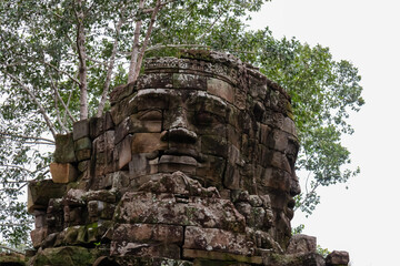 A giant, serene stone face of Avalokiteshvara gazes from a weathered tower top, a mysterious and iconic carving of the Bayon style found in the ancient Khmer temples of Angkor Thom, Siem Reap.