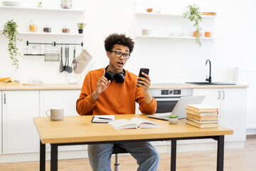 A young man with glasses is on a video call in his kitchen, gesturing with his hand while holding his phone.