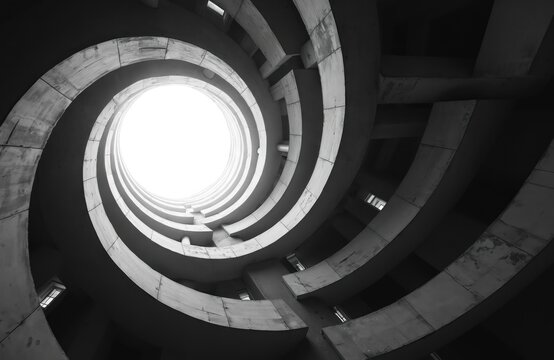 Low angle view shows inside spiral building. White circle opening at top. Black, white picture presents modern architecture with lines, curves abstract design pattern. Geometric style. Building