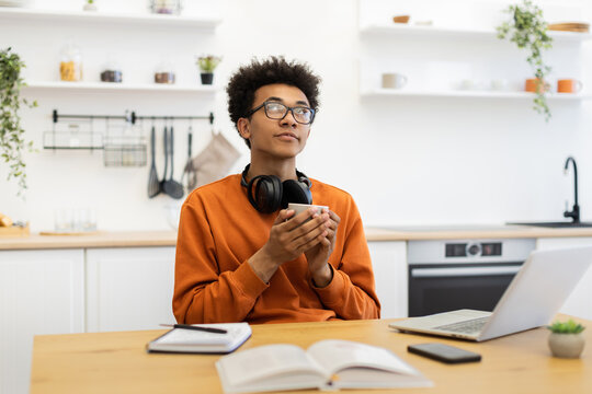 A young man in glasses holds a coffee cup while looking up thoughtfully in a bright kitchen setting. - Powered by Adobe