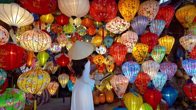 Beautiful Asian woman wearing traditional white ao dai dress with colorful paper lanterns in Hoi An, Vietnam.