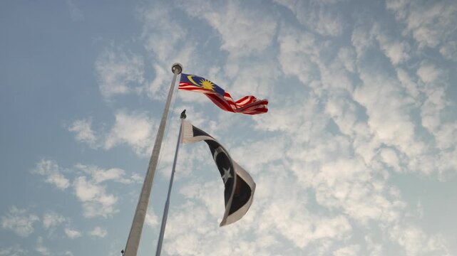 The Jalur Gemilang waves proudly against a bright sky, captured from a dramatic upward angle.