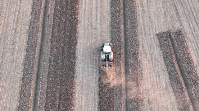 Aerial drone image of a tractor tilling soil in parallel rows during late autumn in the Po Valley, Northern Italy. Dust trails highlight active mechanized farming under clear morning light