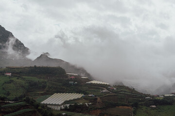 Fototapeta premium Foggy Mountain Valley with Greenhouses and Terraced Fields in Sa Pa, Vietnam