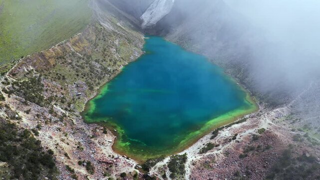 Torquise Laguna Lake Humantay glacier snow capped Humantay trek Peru aerial drone birdseye view rainy season sunny fog clouds high altitude hiking Cusco Peruvian Andes range morning circle left