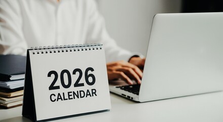 Person working on laptop with a 2026 calendar on a white desk, planning future events and tasks.