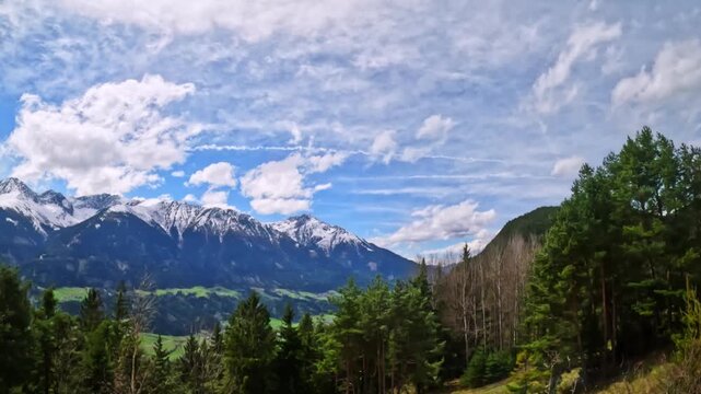 Bright green forests and blossoming spring shrubs stand below the snow-capped Nordkette mountains, with the Inn Valley and Tyrolean hills stretching toward Innsbruck, Austria.