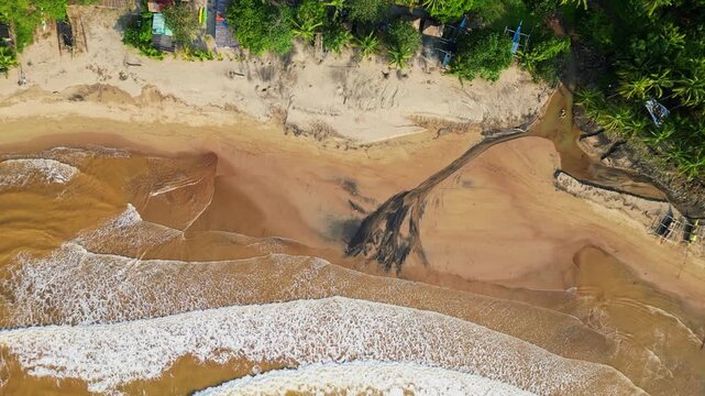 Rising top‑view aerial highlighting black sand patterns along the shoreline as waves roll onto the coast, framed by lush tropical scenery at Quinawan Beach in Mariveles, Bataan, Philippines.