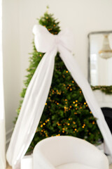 Decorated Christmas tree with glowing lights and a large white bow, soft interior setting.