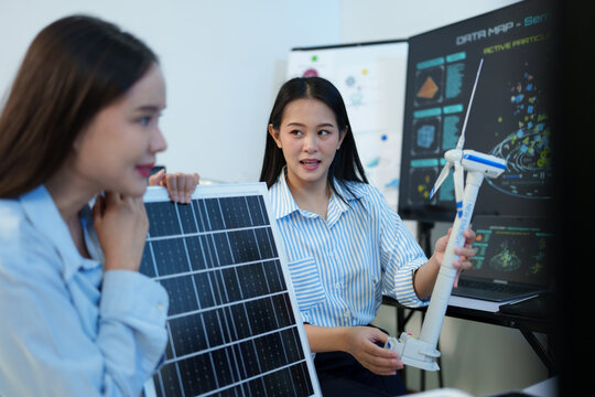 A female engineer is sitting and checking the operation of solar panels and wind turbines in the office.