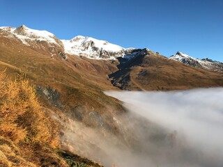 Late Autumn Landscape in the Engadin Swiss Alps with Golden Mountain Slopes, Morning Mist, Deep Blue Alpine Sky and snowcapped mountains 