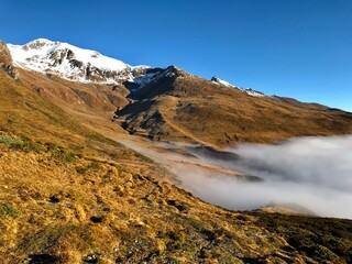Late Autumn Landscape in the Engadin Swiss Alps with Golden Mountain Slopes, Morning Mist, Deep Blue Alpine Sky and snowcapped mountains 