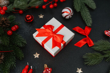 Naklejka premium Gift box with red ribbon, pine branches, berries and festive decorations on dark surface