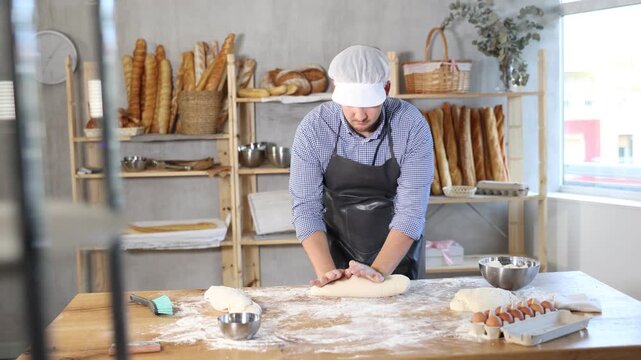 Guy works as baker in bakery, molds sausages from dough, rolls long round strips from dough. Working moment, process of creating croissants in bakery