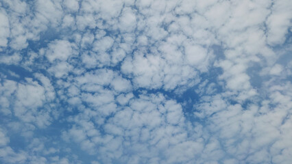 Blue sky covered in scattered, patchy white altocumulus clouds in November as cloudscape background 