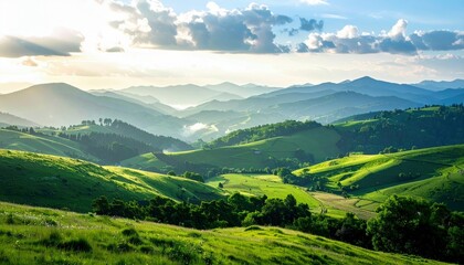 Fototapeta premium A vast landscape of layered green hills and mountains under a bright, cloudy sky, with sunlight illuminating the terrain.