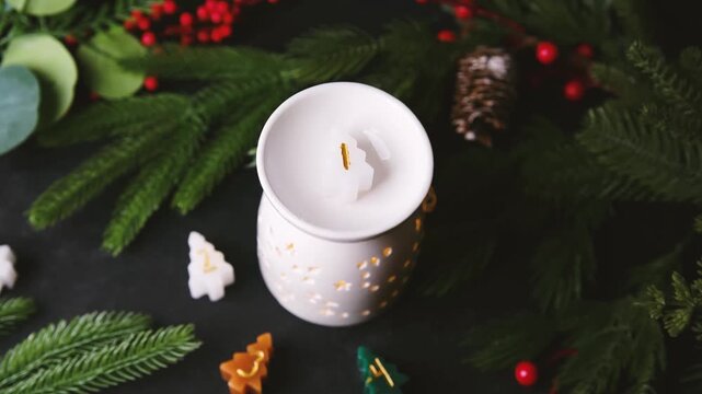 Winter scent diffuser with small tree shaped candles and pine needles on dark surface.