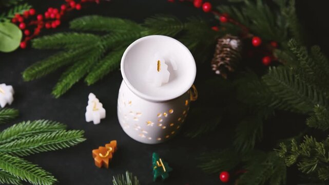 Christmas tree candles burning in a warm ceramic diffuser with pine needles and red berries