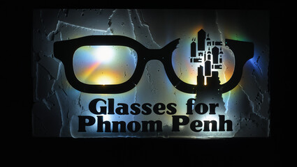 Glasses for phnom penh a vision support initiative.
A sign with large, black glasses outlines is illuminated with colorful lighting effects. "Glasses for Phnom Penh" is written below the glasses.