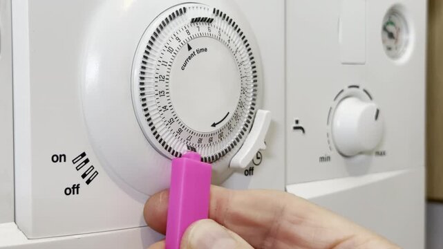 Closeup of a man&rsquo;s hand selecting a segment of tabs on a manual programmer, to set the activation period for a domestic gas boiler for heating and hot water.