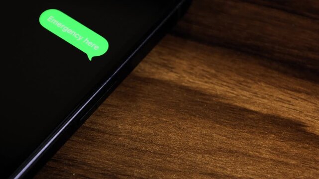 Close-up view of a smartphone screen showing an outgoing &ldquo;Emergency Here, Need Help Now&rdquo; text message in a green bubble, captured as it sends with a smooth popup animation.