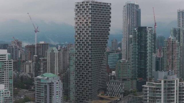 Telephoto panning aerial shot of the unique skyscraper Vancouver House architecture on a rainy afternoon in British Columbia, Canada. 4K